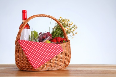 Photo of Picnic basket with wine and products on wooden table against white background. Space for text