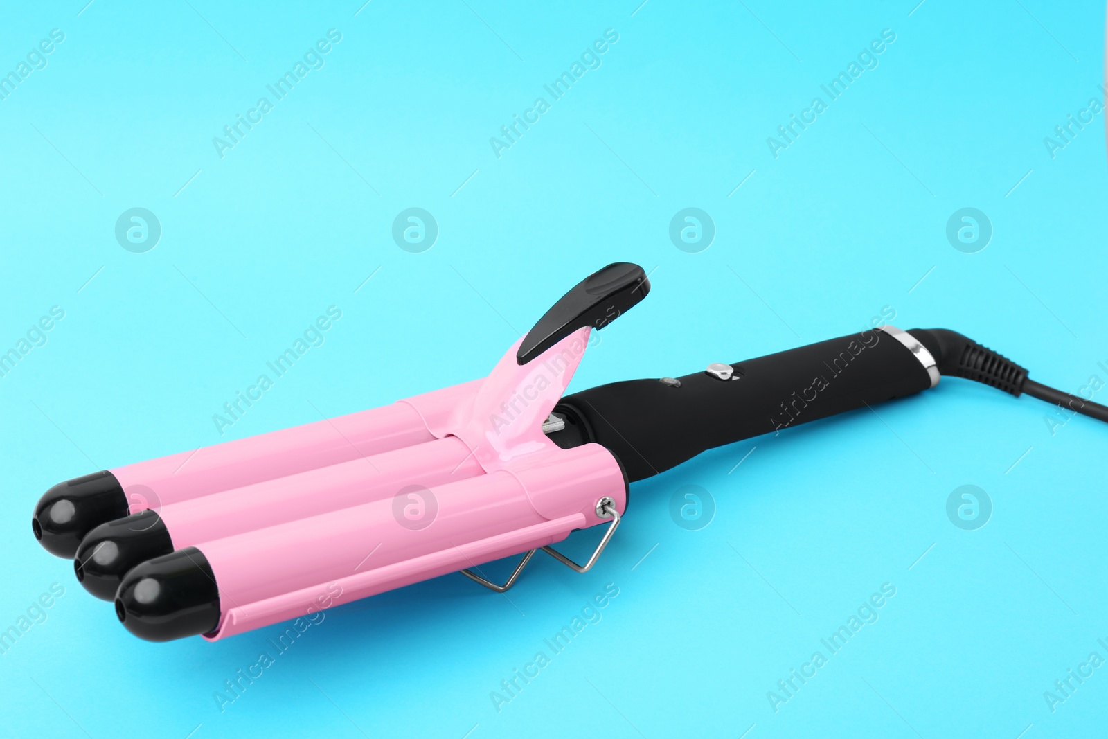 Photo of Modern triple curling iron on light blue background