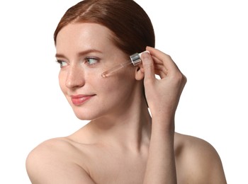 Beautiful woman with freckles applying cosmetic serum onto her face on white background