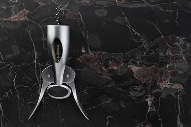 Photo of One wing corkscrew on black marble table, top view. Space for text