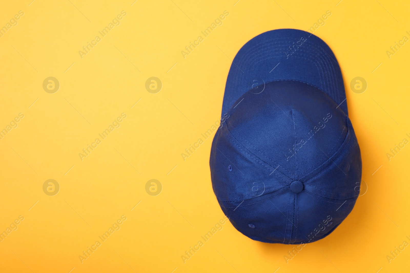 Photo of Stylish blue baseball cap on yellow background, top view. Space for text