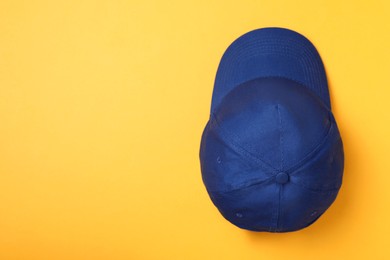 Photo of Stylish blue baseball cap on yellow background, top view. Space for text