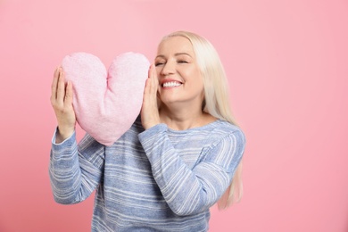 Photo of Portrait of mature woman with decorative heart shaped pillow on color background