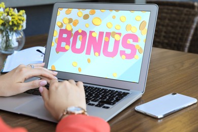 Image of Bonus gaining. Woman using laptop at wooden table indoors, closeup. Illustration of falling coins and word on device screen