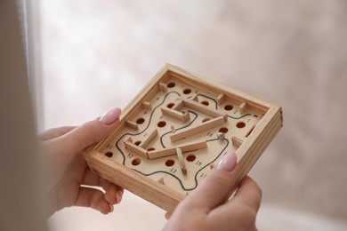 Woman holding wooden toy maze with metal ball on blurred background, closeup