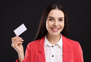 Happy woman holding blank business card on black background