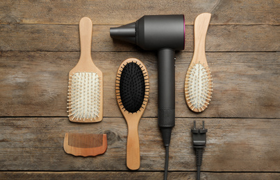 Photo of Hair dryer and different brushes on wooden table, flat lay. Professional hairdresser tool