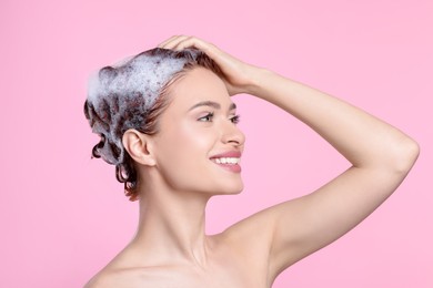 Happy young woman washing her hair with shampoo on pink background