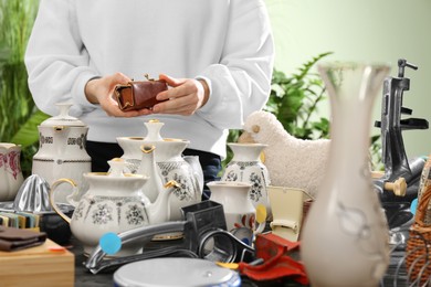 Photo of Woman holding vintage wallet above table with different stuff indoors, closeup. Garage sale