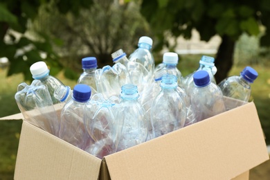 Photo of Cardboard box with used plastic bottles outdoors. Recycle concept