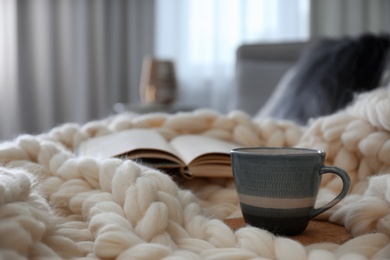 Photo of Cup of coffee and book on white knitted plaid indoors