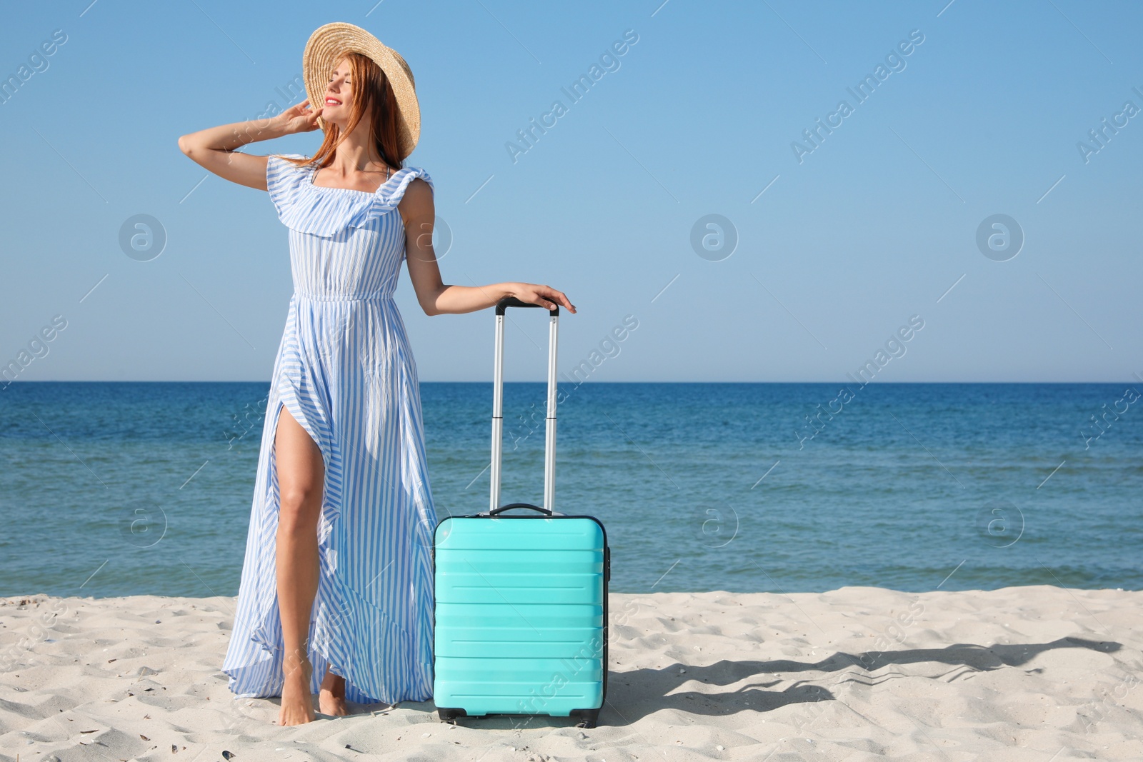 Photo of Beautiful woman with suitcase on sandy beach near sea