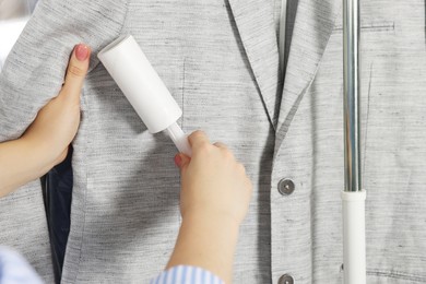 Woman using adhesive lint roller indoors, closeup. Dry-cleaning service