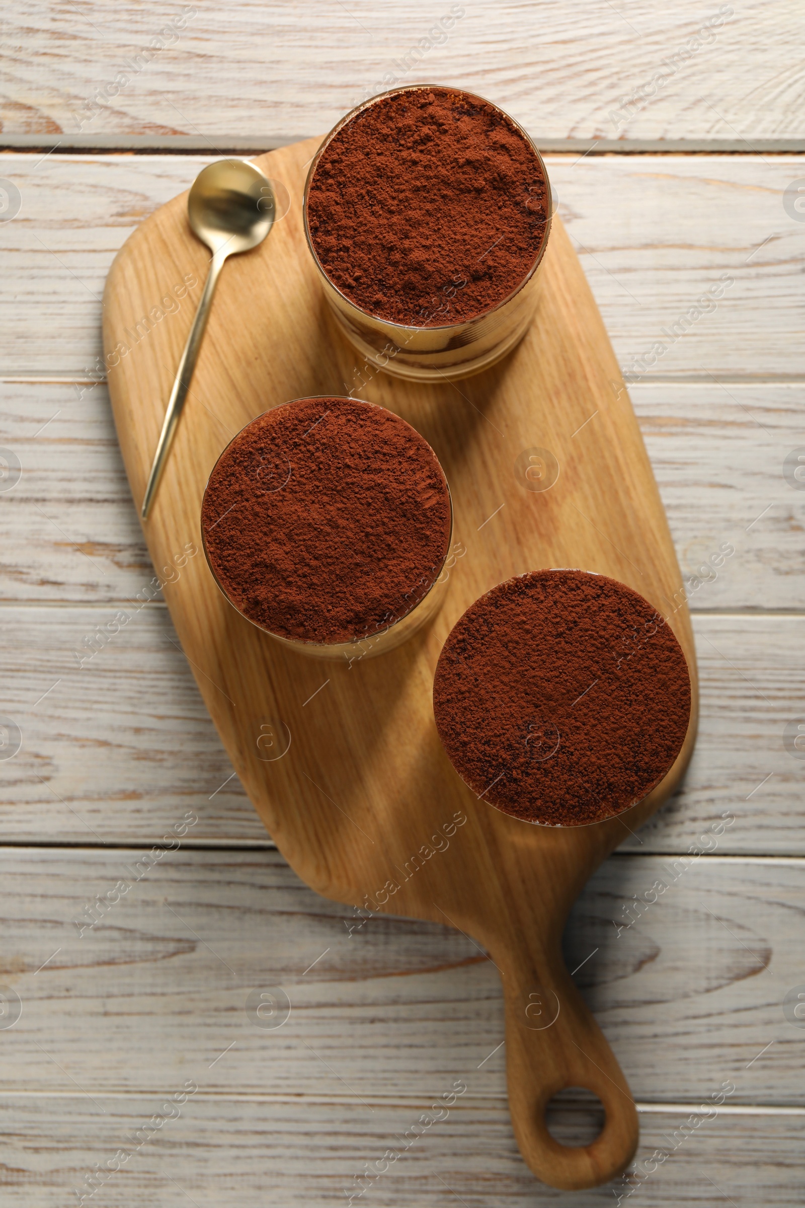 Photo of Delicious tiramisu in glasses and spoon on light wooden table, top view