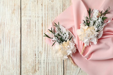 Photo of Stylish boutonnieres and pink fabric on light wooden table, top view. Space for text