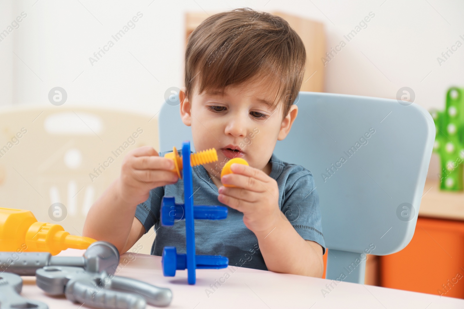 Photo of Little child playing with toy construction tools at table