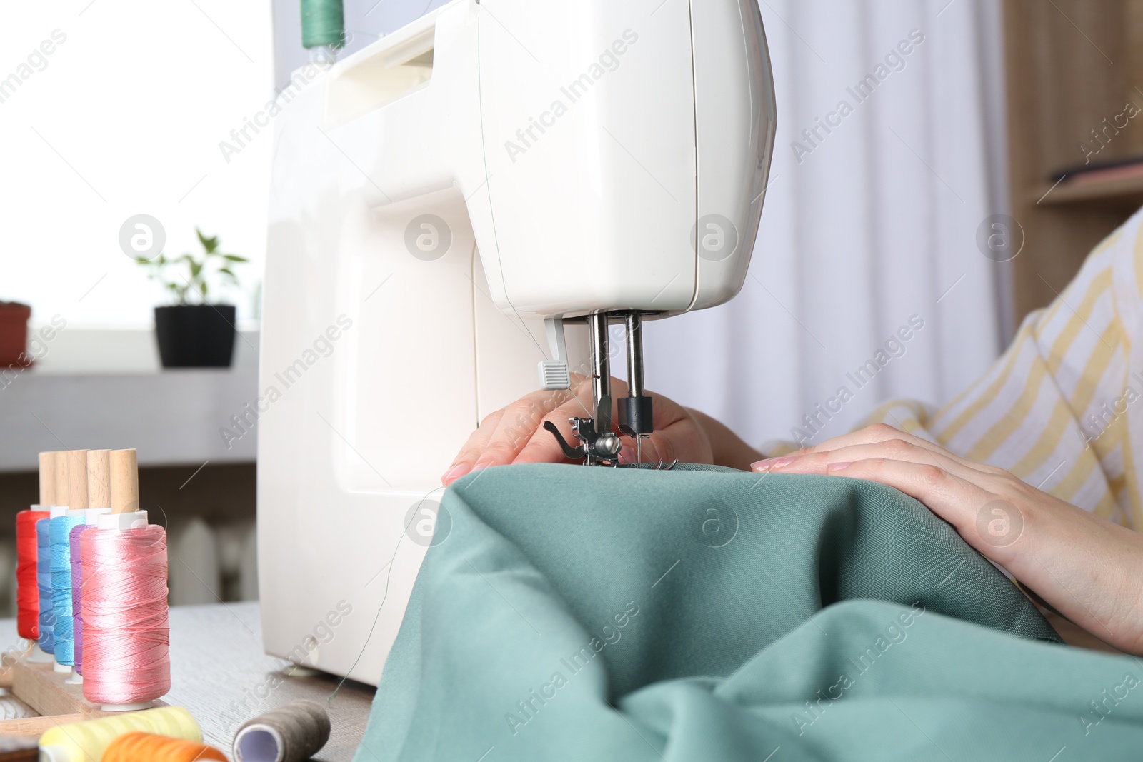 Photo of Seamstress working with sewing machine at table indoors, closeup