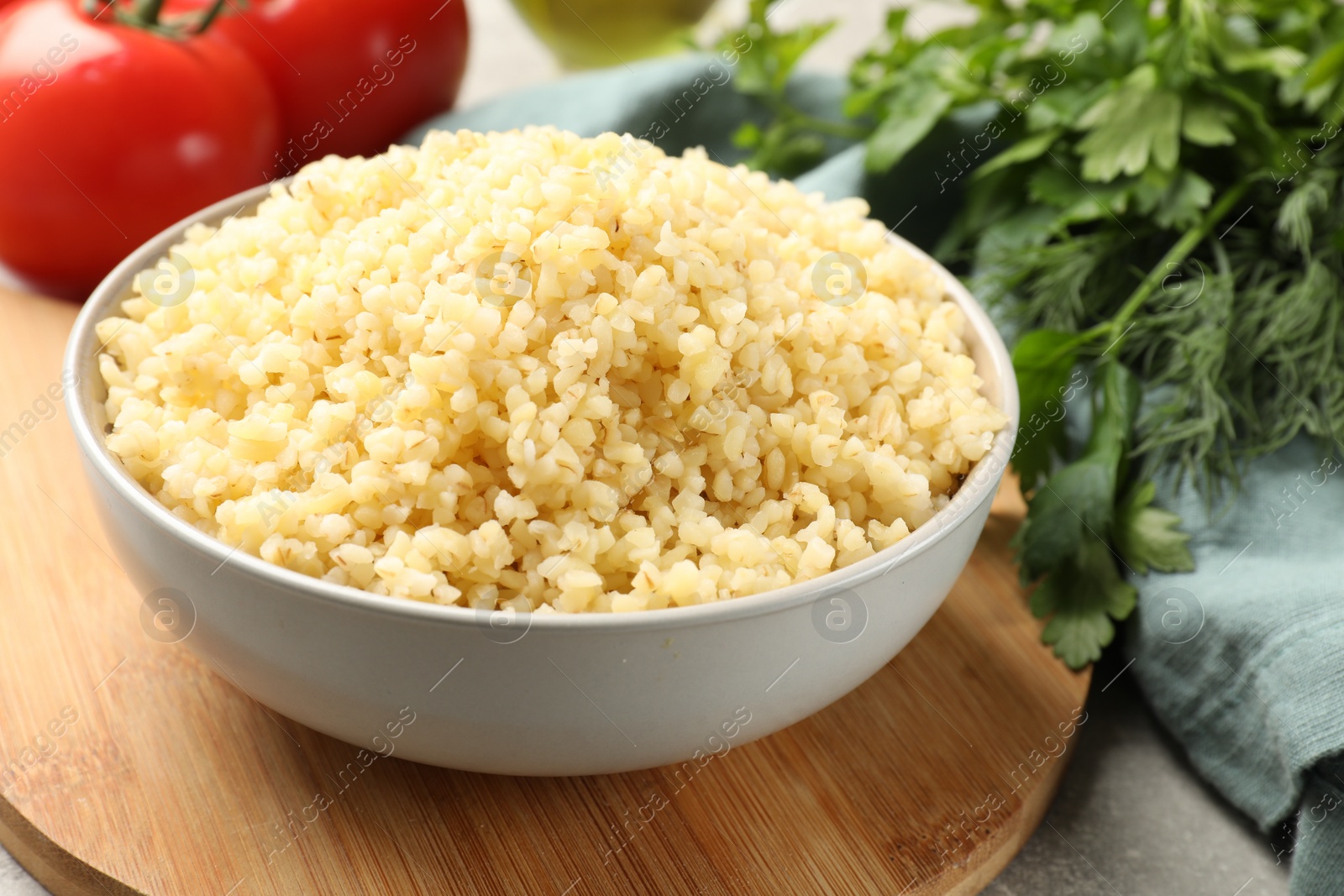 Photo of Delicious bulgur in bowl, greens and tomatoes on table, closeup