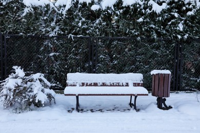 Trash bin and wooden bench covered with snow in morning park