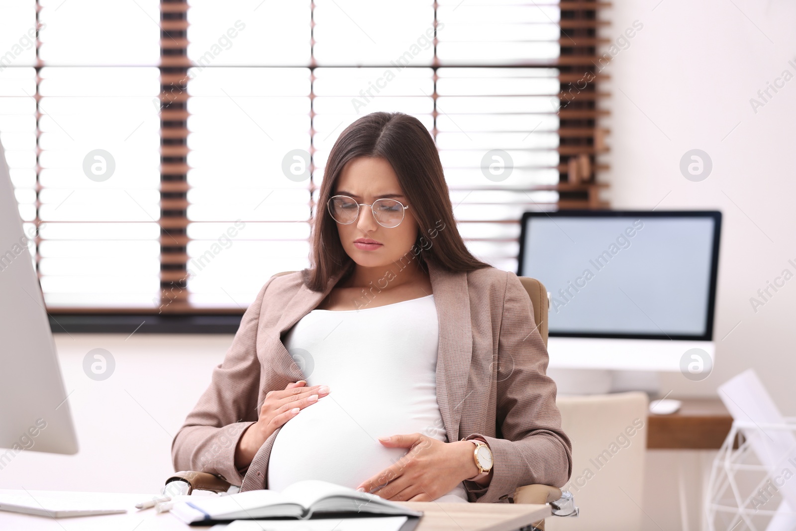 Photo of Young pregnant woman suffering from pain while working in office