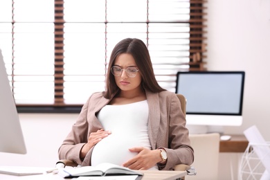 Photo of Young pregnant woman suffering from pain while working in office