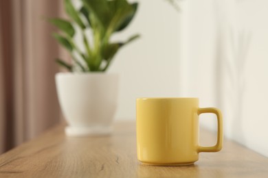 Photo of Yellow mug on wooden table indoors. Mockup for design