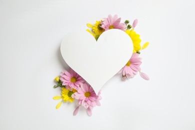 Beautiful chamomile flowers and heart shaped paper card on white background, flat lay with space for text