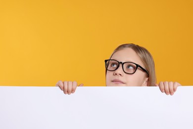 Photo of Cute girl looking out of placard against orange background. Space for text