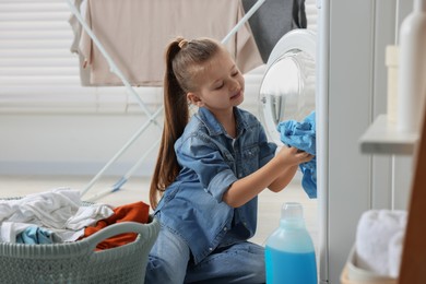 Photo of Little girl putting dirty clothes into washing machine in bathroom