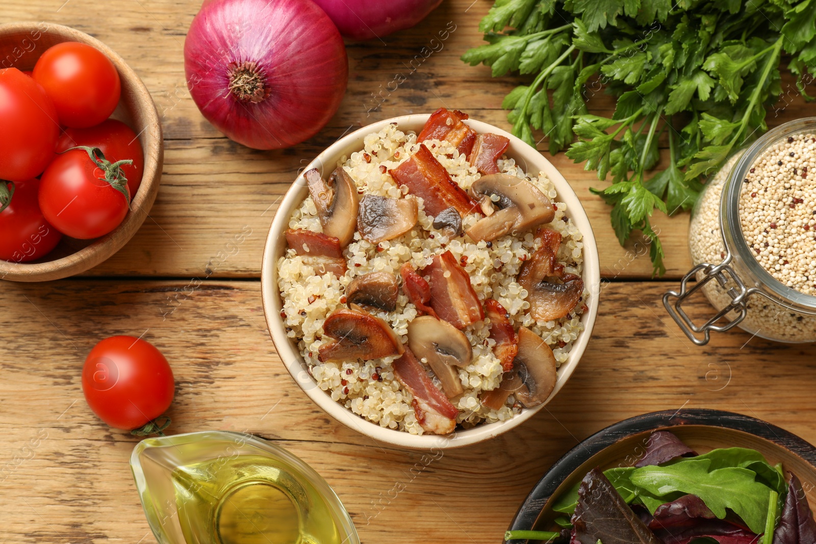 Photo of Tasty quinoa porridge with fried bacon, mushrooms in bowl and vegetables on wooden table, flat lay