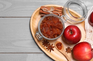 Photo of Delicious apple jam in jar, fresh fruits and spices on grey wooden table, flat lay. Space for text