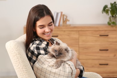 Woman hugging her cute cat on soft armchair at home
