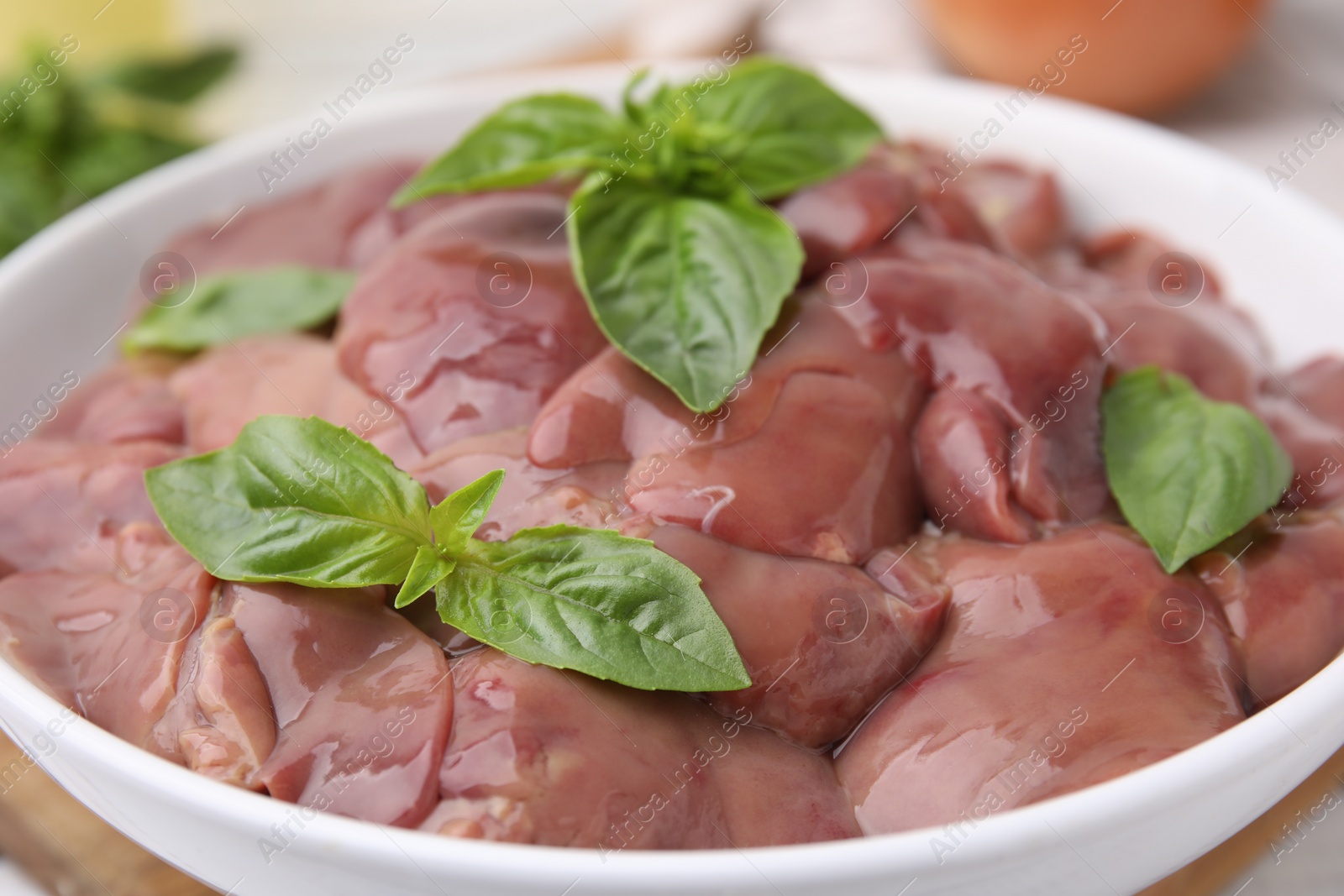 Photo of Bowl with raw chicken liver and basil on table, closeup