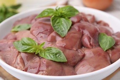 Photo of Bowl with raw chicken liver and basil on table, closeup
