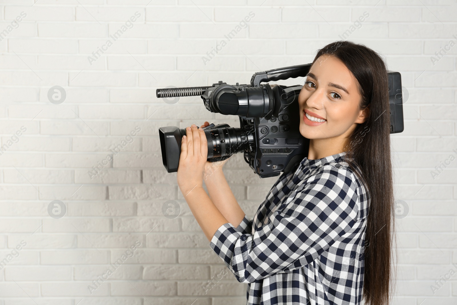 Photo of Operator with professional video camera near white brick wall