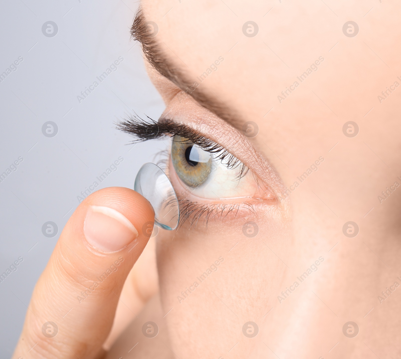 Photo of Young woman putting contact lens in her eye, closeup