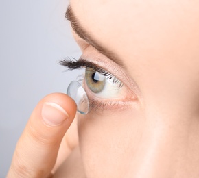 Photo of Young woman putting contact lens in her eye, closeup