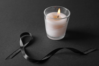 Photo of Black ribbon and burning candle on dark background. Funeral symbols