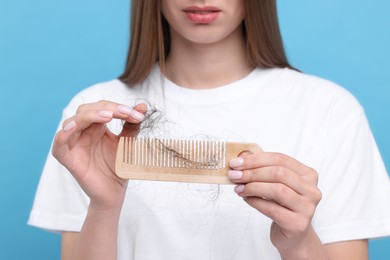 Photo of Woman untangling her lost hair from comb on light blue background, closeup. Alopecia problem