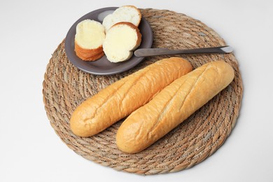 Photo of Whole and cut baguettes with fresh butter on white table, above view