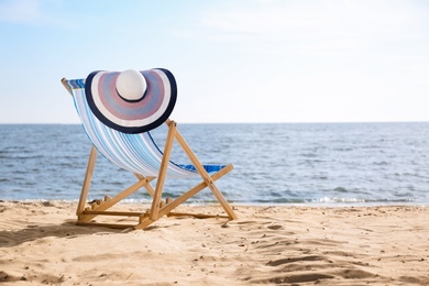 Lounger and hat on sand near sea, space for text. Beach objects