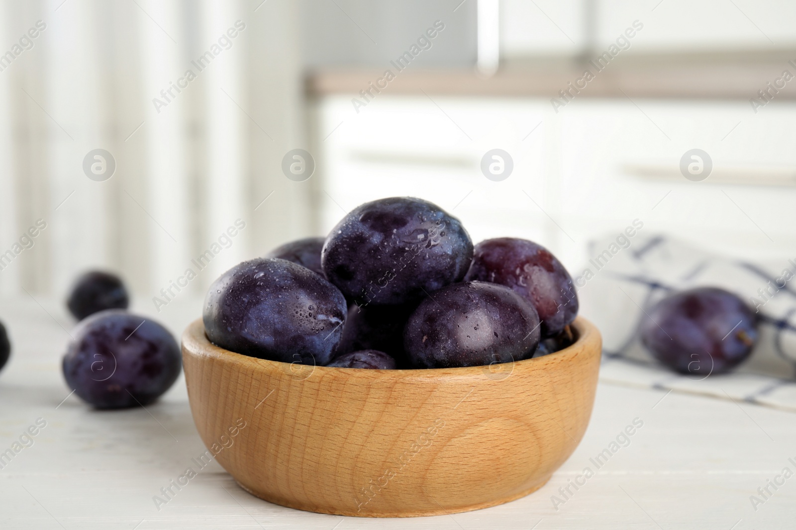 Photo of Delicious ripe plums in wooden bowl on white table