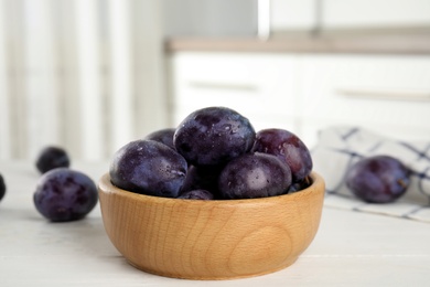 Delicious ripe plums in wooden bowl on white table