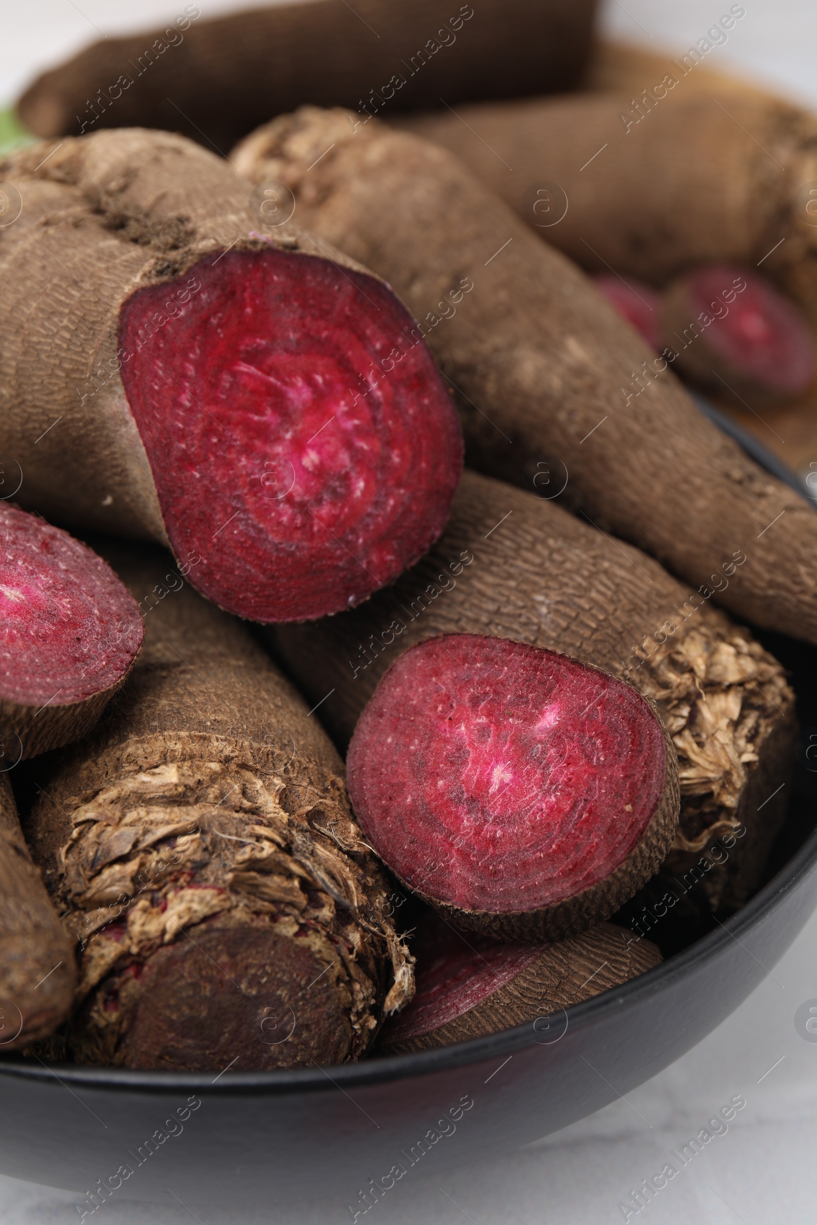 Photo of Whole and cut red beets in bowl on table, closeup