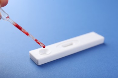 Photo of Woman dropping blood sample onto disposable express test cassette with pipette on blue background, closeup