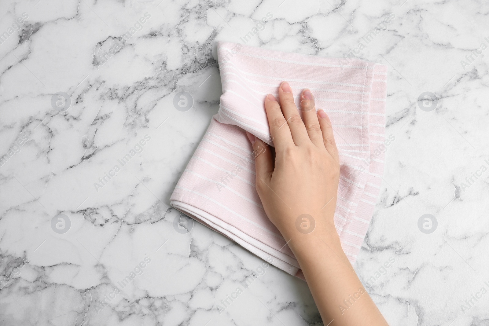 Photo of Woman wiping white marble table with kitchen towel, top view