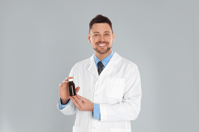 Professional pharmacist with syrup on light grey background