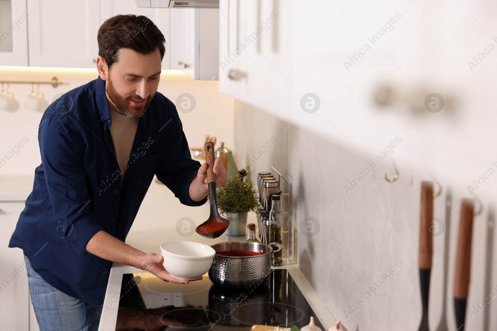 Photo of Man pouring delicious tomato soup into bowl in kitchen