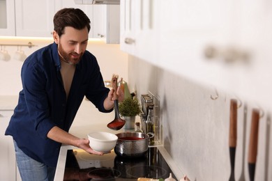 Man pouring delicious tomato soup into bowl in kitchen