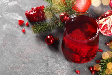 Aromatic Sangria drink in glass, Christmas decor and pomegranate grains on grey textured table, space for text